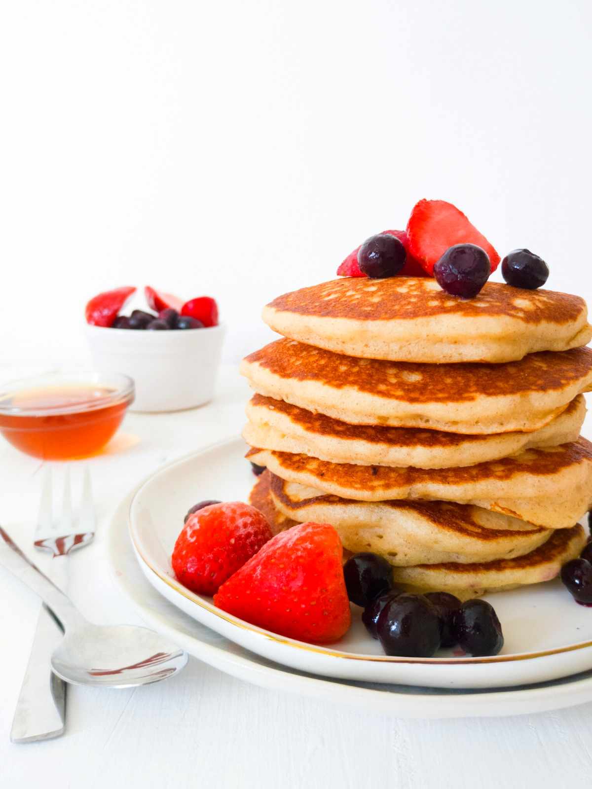 Gluten-free sourdough pancakes on a white plate with strawberries and blueberries.