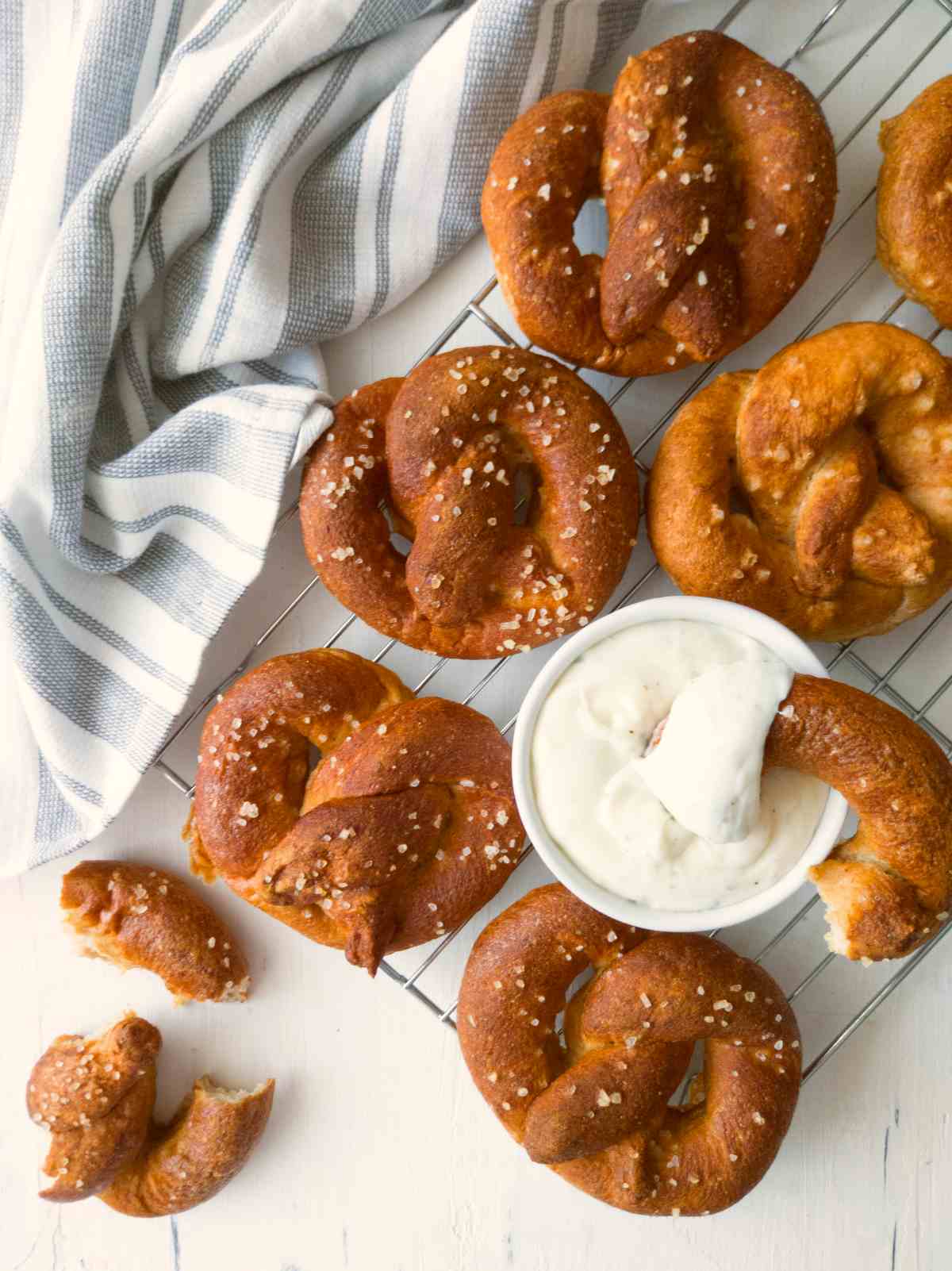 Gluten-free sourdough soft pretzels on a cooling rack with sauce and a towel in the background.