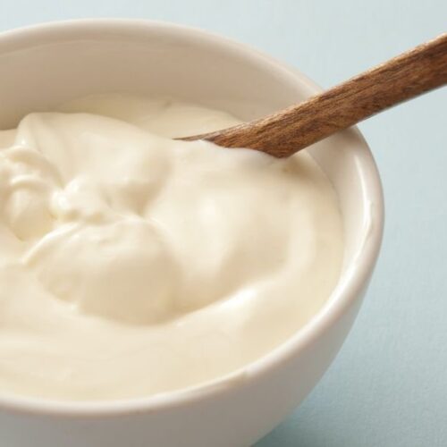 Homemade Mayonnaise in a white bowl with a wooden spoon immersed in it.