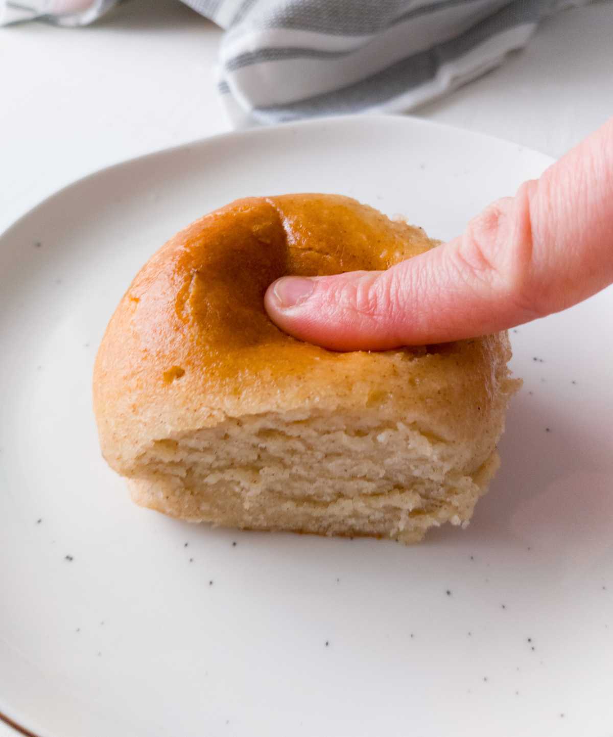 Pressing down a dinner roll with a finger.