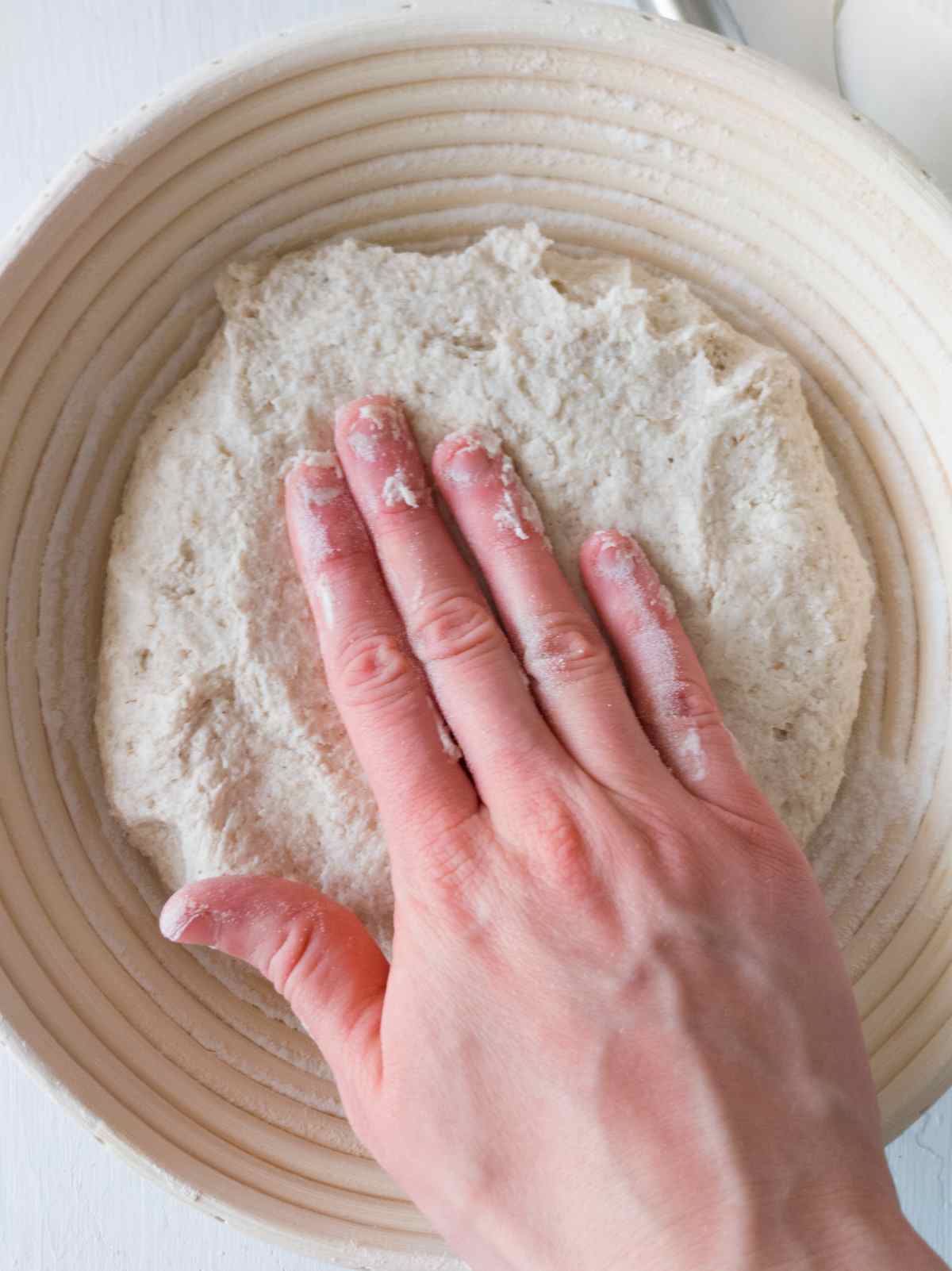 Pressing the dough into a banneton basket with a hand.