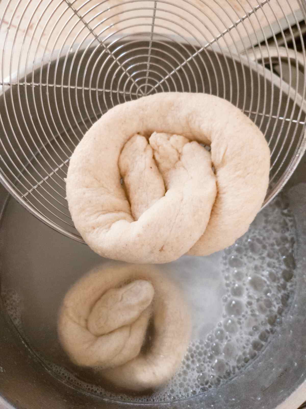 A pretzel in a spider strainer over a water bath.