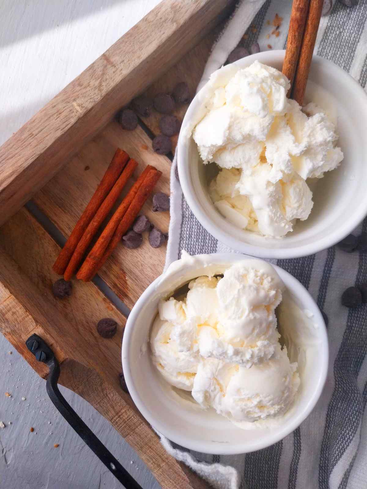 2 small white bowls on a wooden tray with cinnamon sticks next to it.