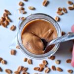 Blender peanut butter being scooped by a small spoon from a glass jar.