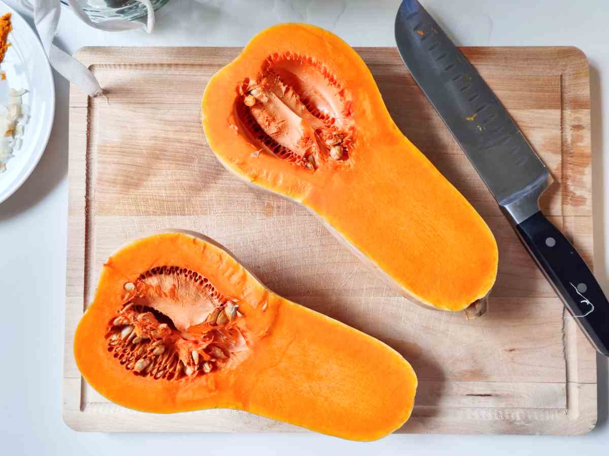 Halved pumpkin on a cutting board with a large knife next to it.