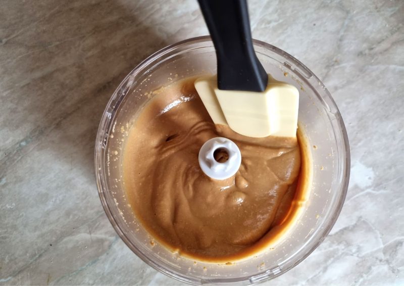 Creamy and runny peanut butter in the blending cup with a rubber spatula in it.