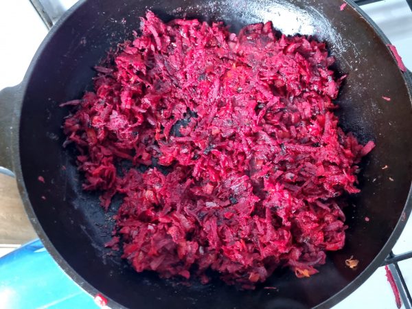 Frying red beets, carrots, and onions in a cast iron pan.