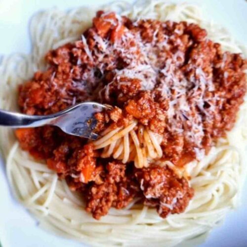 Spaghetti Bolognese on a plate with a fork scooping it up.