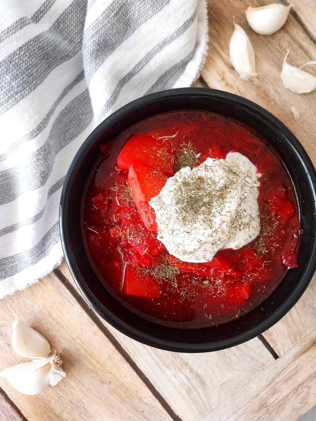 Ukrainian borscht in a black bowl with a dollop of sour cream on the top.
