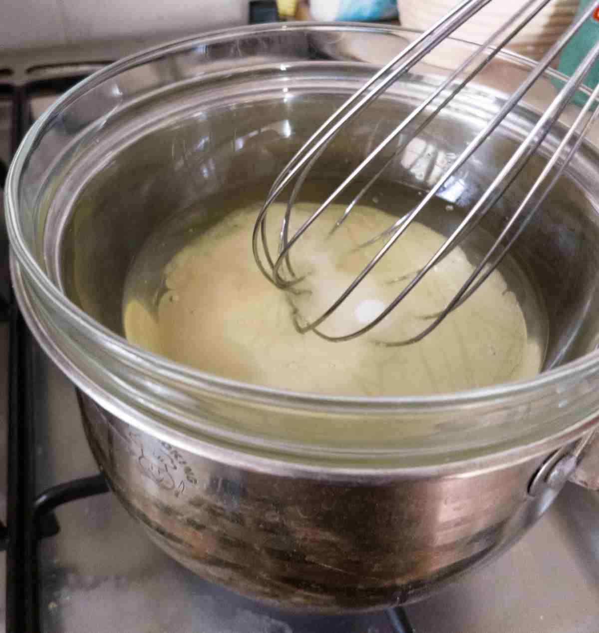 Double boiler with a glass bowl over a metal saucepan with a whisk in it. 