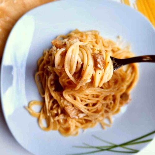 Spaghetti carbonara on a plate scooped up with a fork.
