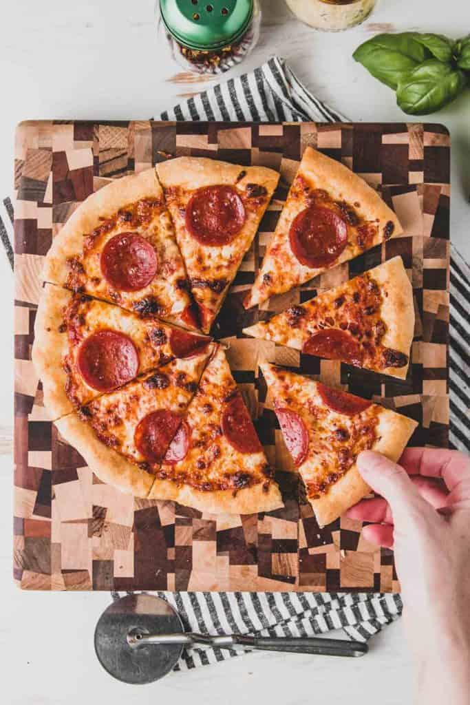 Caputo Fioreglot pepperoni pizza sliced with a hand taking a slice. 
