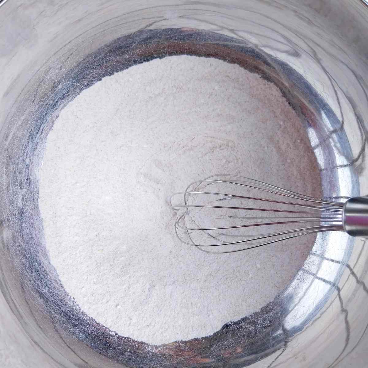 Dry ingredients in a metal mixing bowl with a whisk.