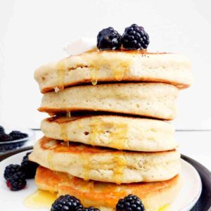 A stack of buckwheat pancakes with blackberries and honey dripping from the top.