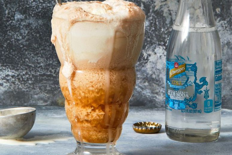 Ice cream float in a large glass with a bottle of sode in the background.