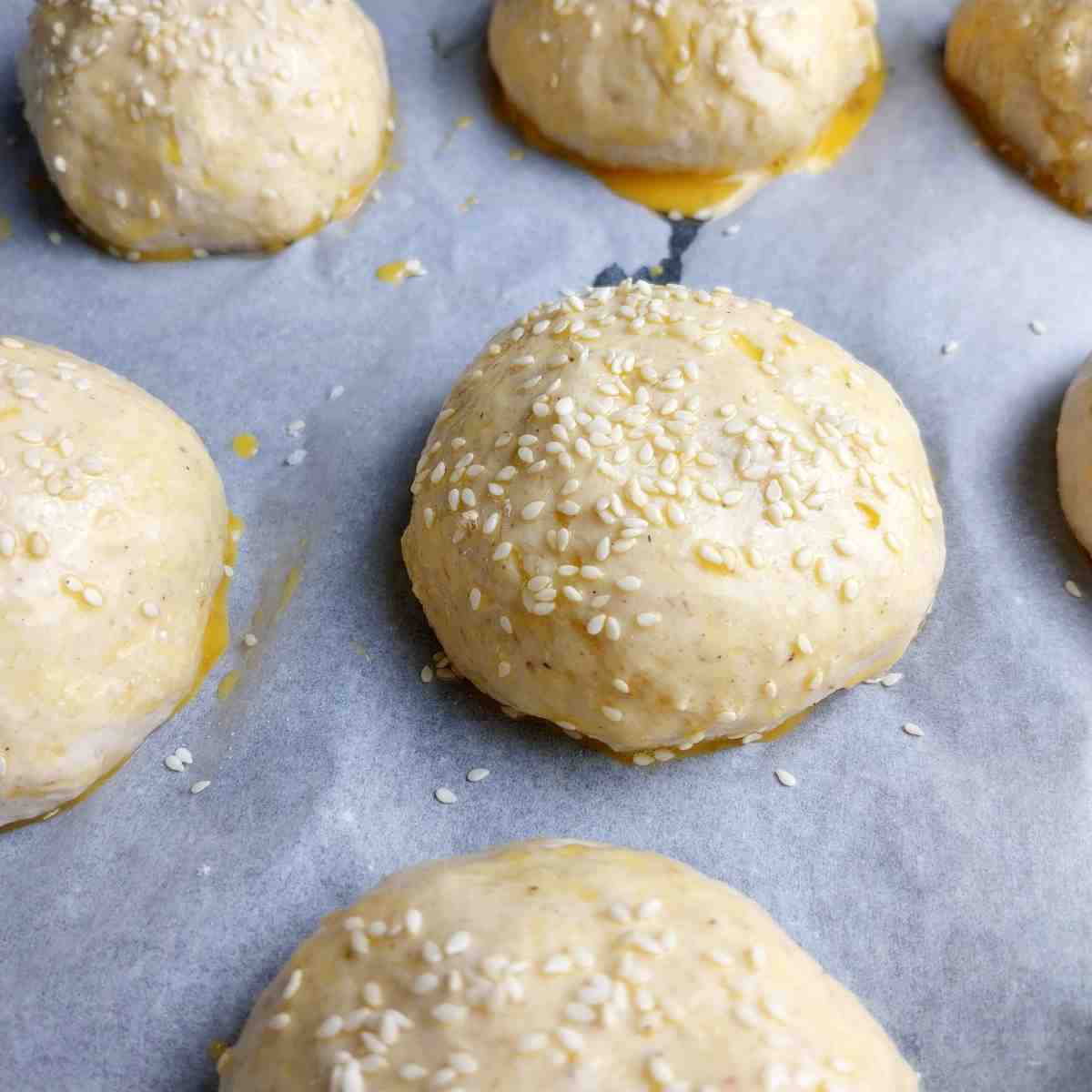 Buns brushed with egg wash and topped with sesame seeds.