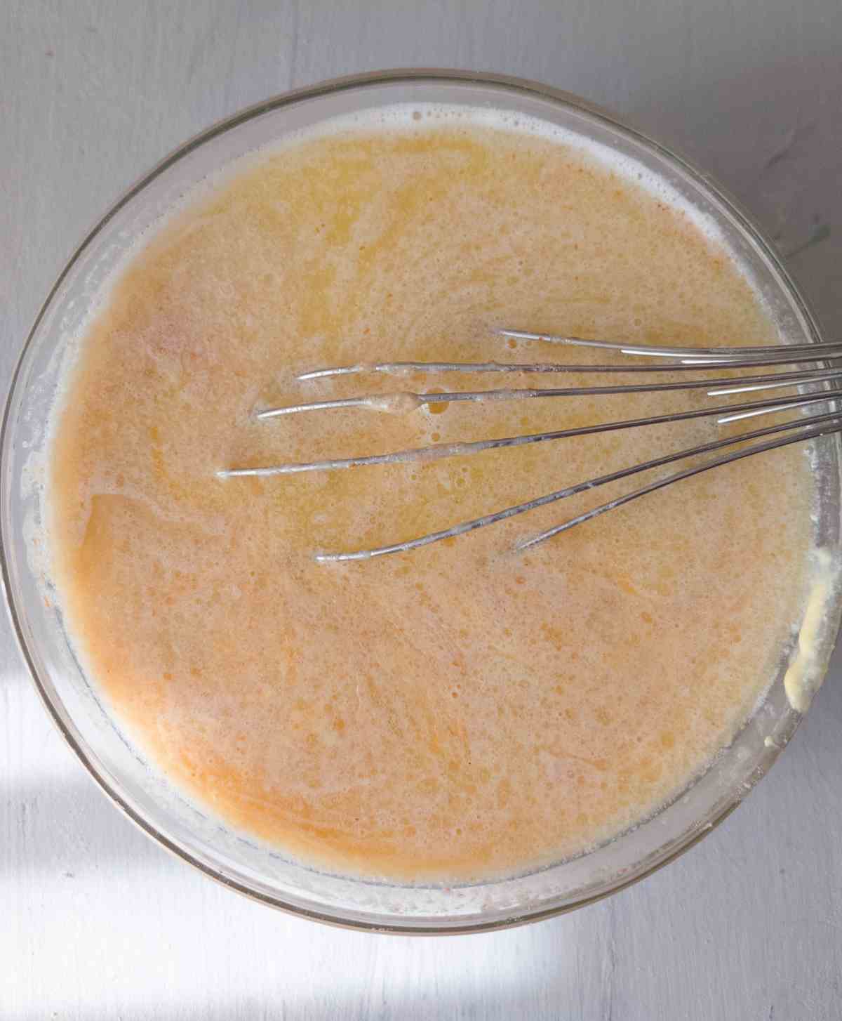 Wet ingredients in a glass bowl with a whisk.
