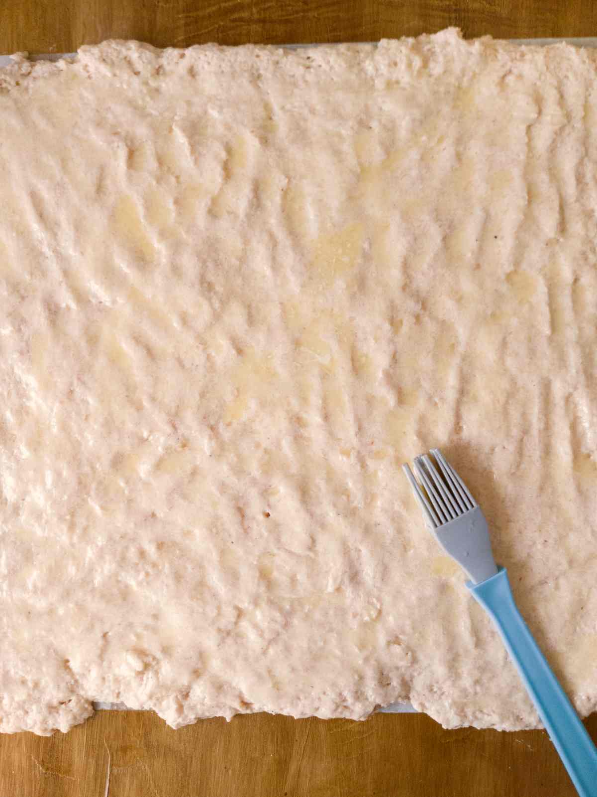 Spreading melted butter onto the rolled out dough with a silicone brush.