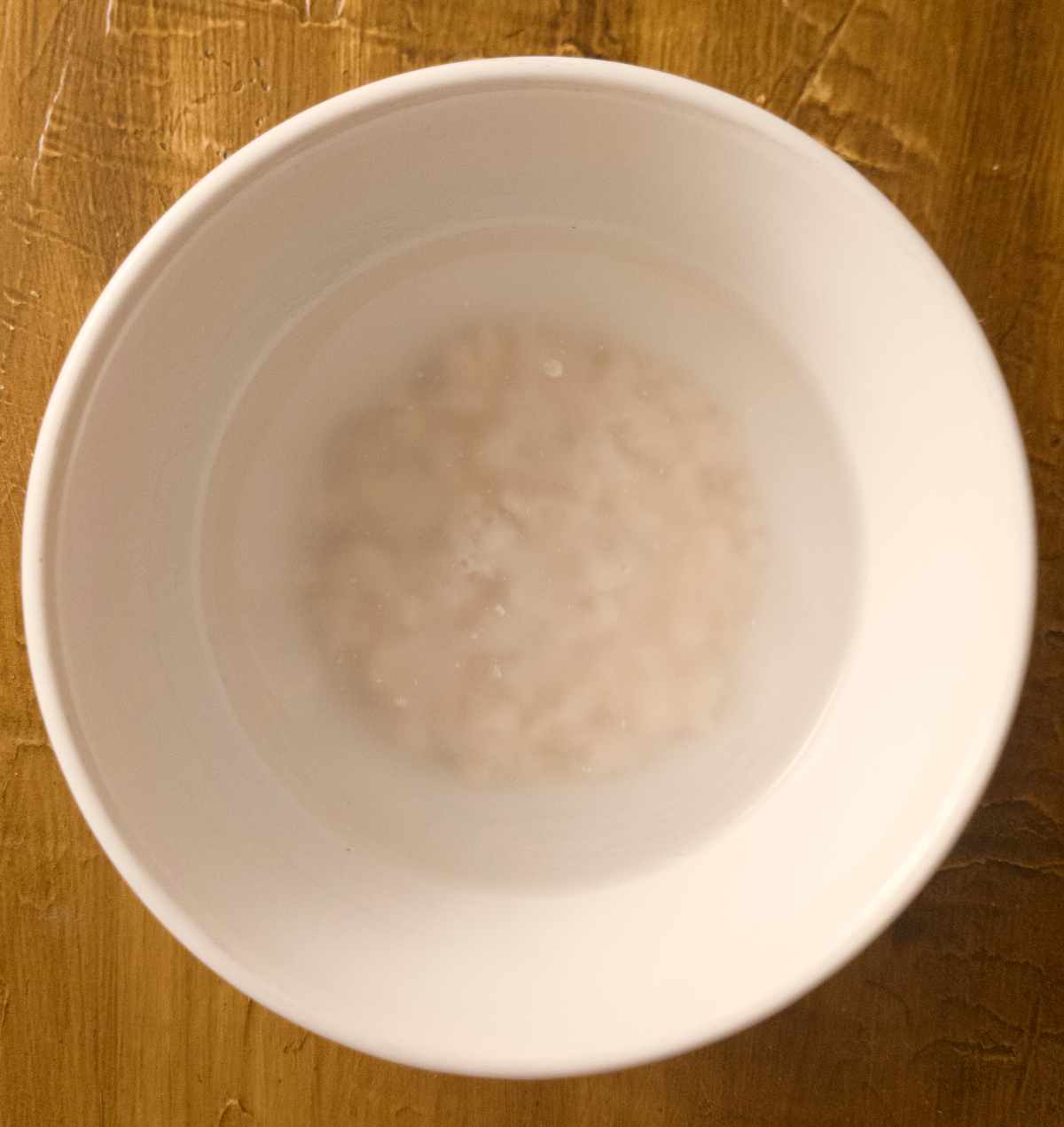 Yeast in water in a white bowl on a wooden surface.