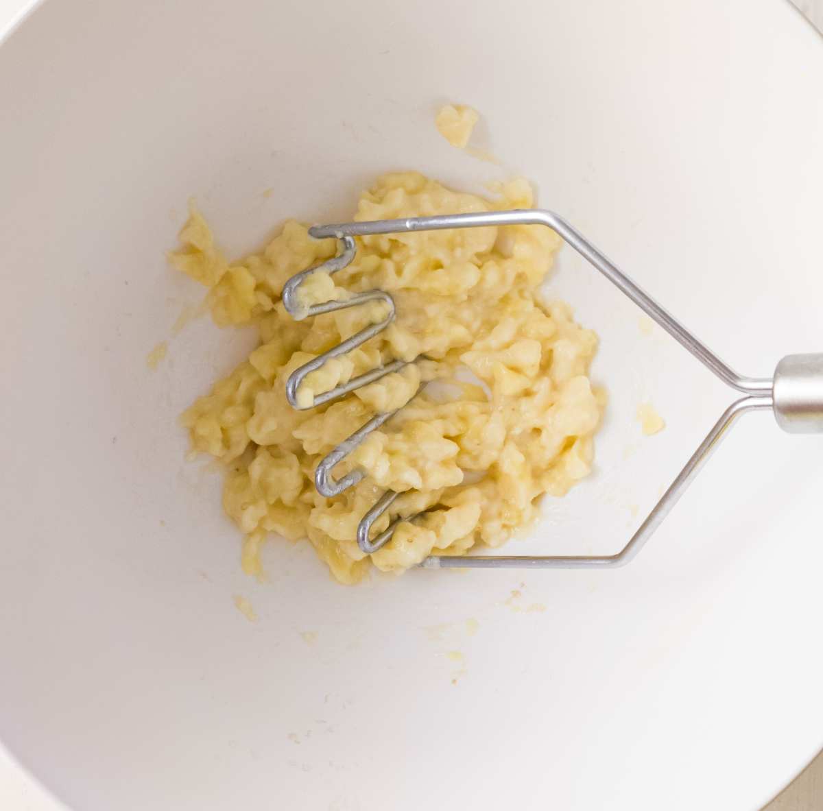 Mashed bananas in a bowl with a potato masher.