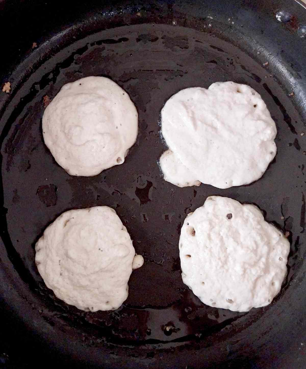 Crumpet dough frying in a cast iron pan.