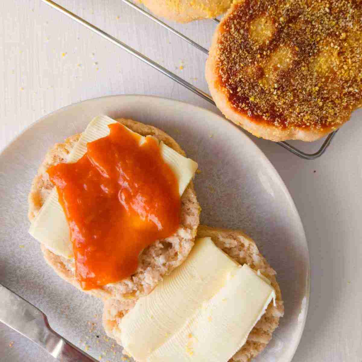 Gluten-free sourdough English muffin cut in half on a plate with butter and jam.