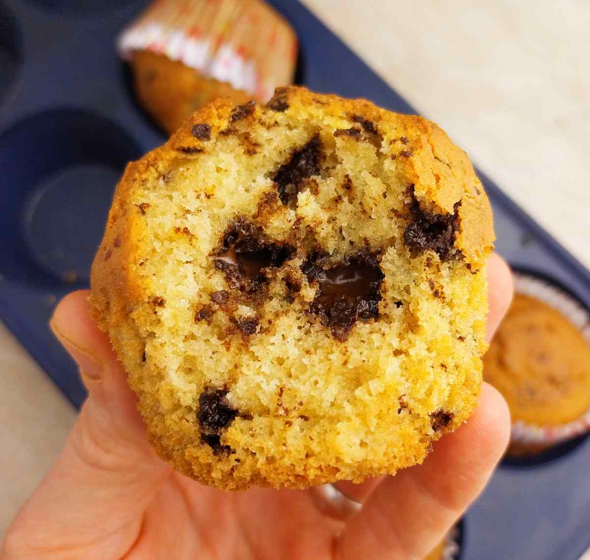 Rice flour muffin held in a hdn with a blue muffin tin in the background on a light surface.