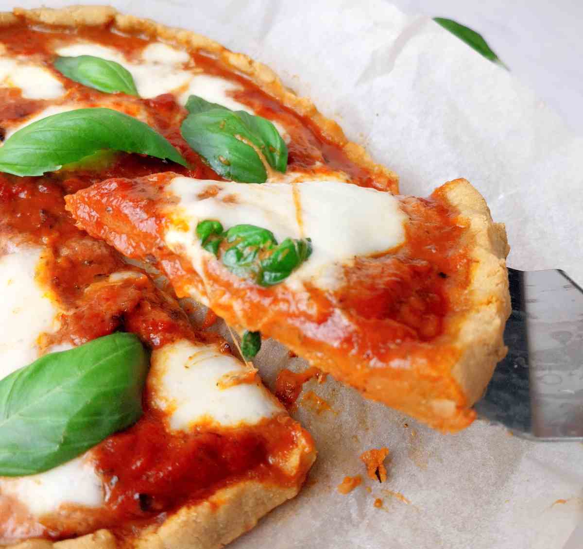 A slice of cassava flour pizza on a serving spatula with the rest of the pizza in the background.