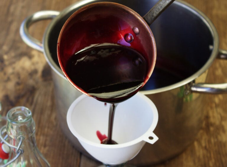 Pouring the elderberry vinegar with a ladle into a funnel.