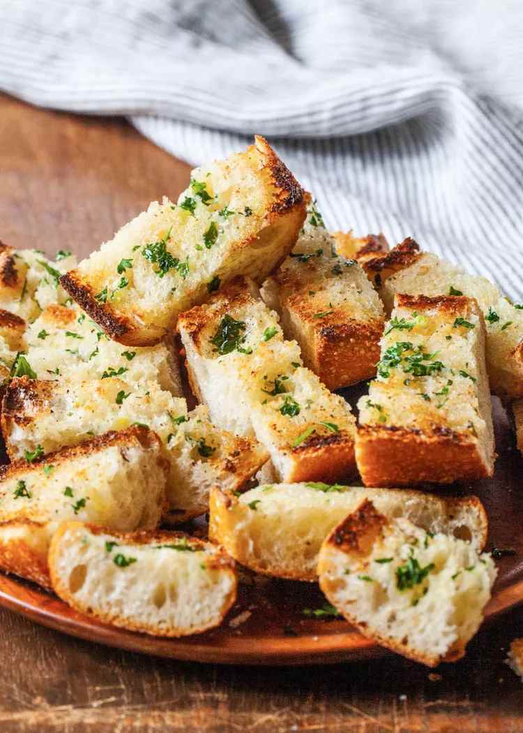 Garlic bread slices on a wooden surface with a towel in the background.