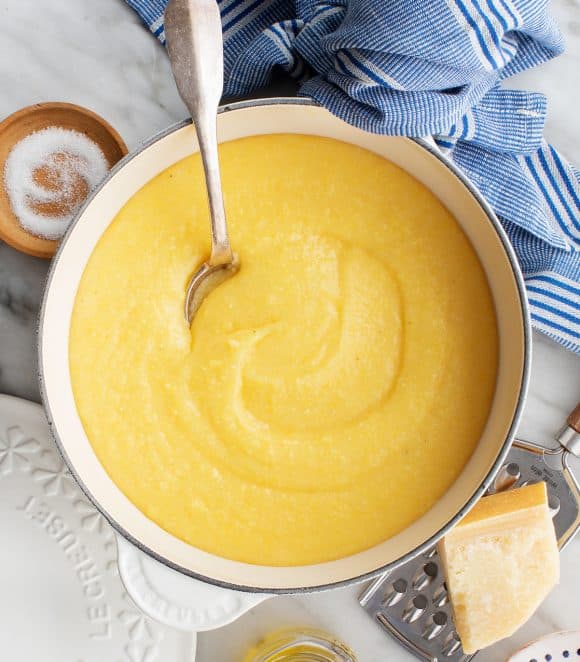 Creamy polenta in a bowl with a spoon and a tea towel in the background.