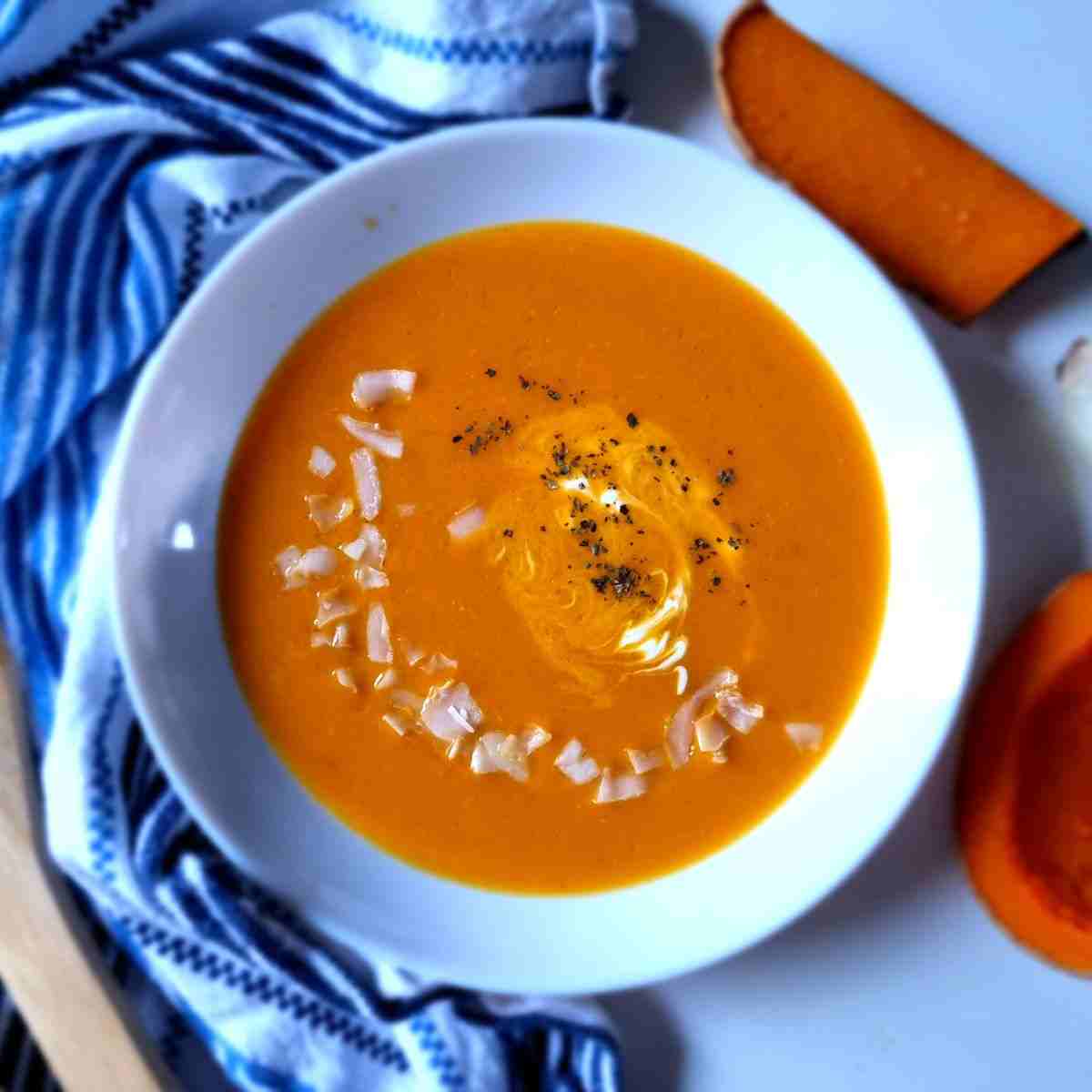 Pumpkin soup in a white bowl with a kitchen towel on the side.