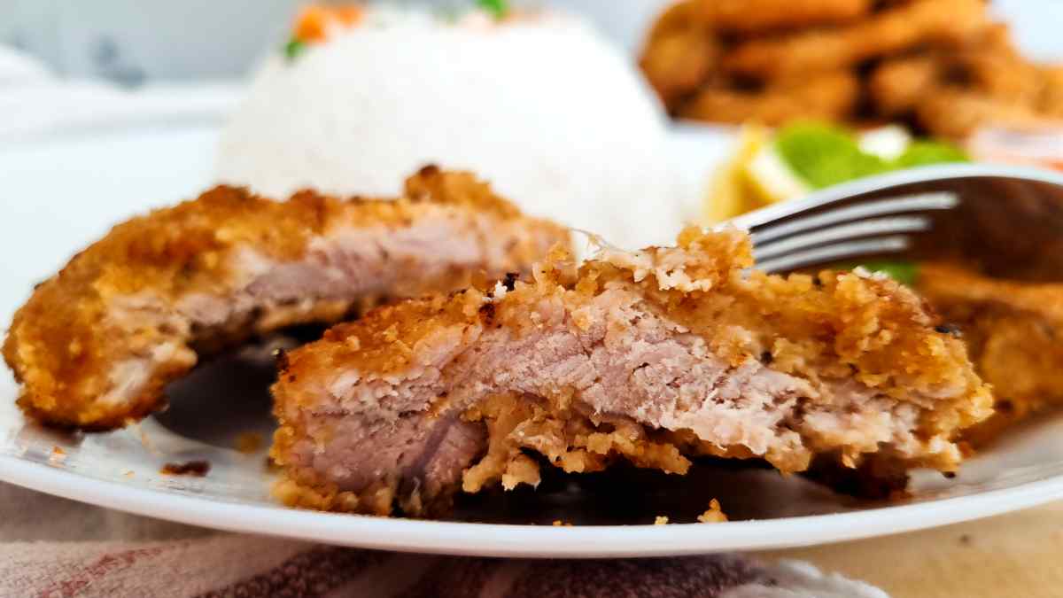 Cut in half gluten free pork cutlets on a place with a fork.