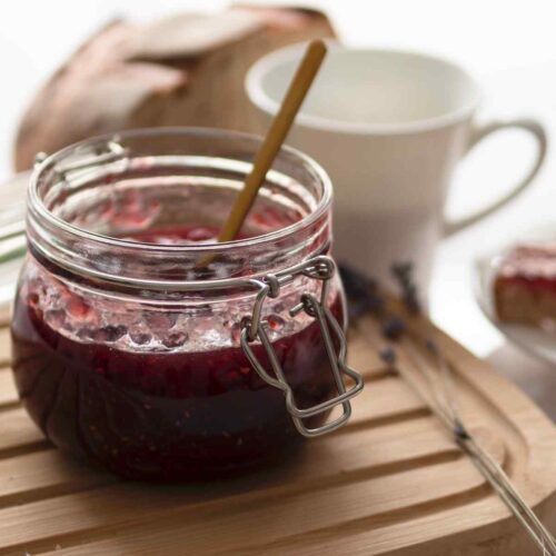 Plum jam in a little jar with a wooden spoon.