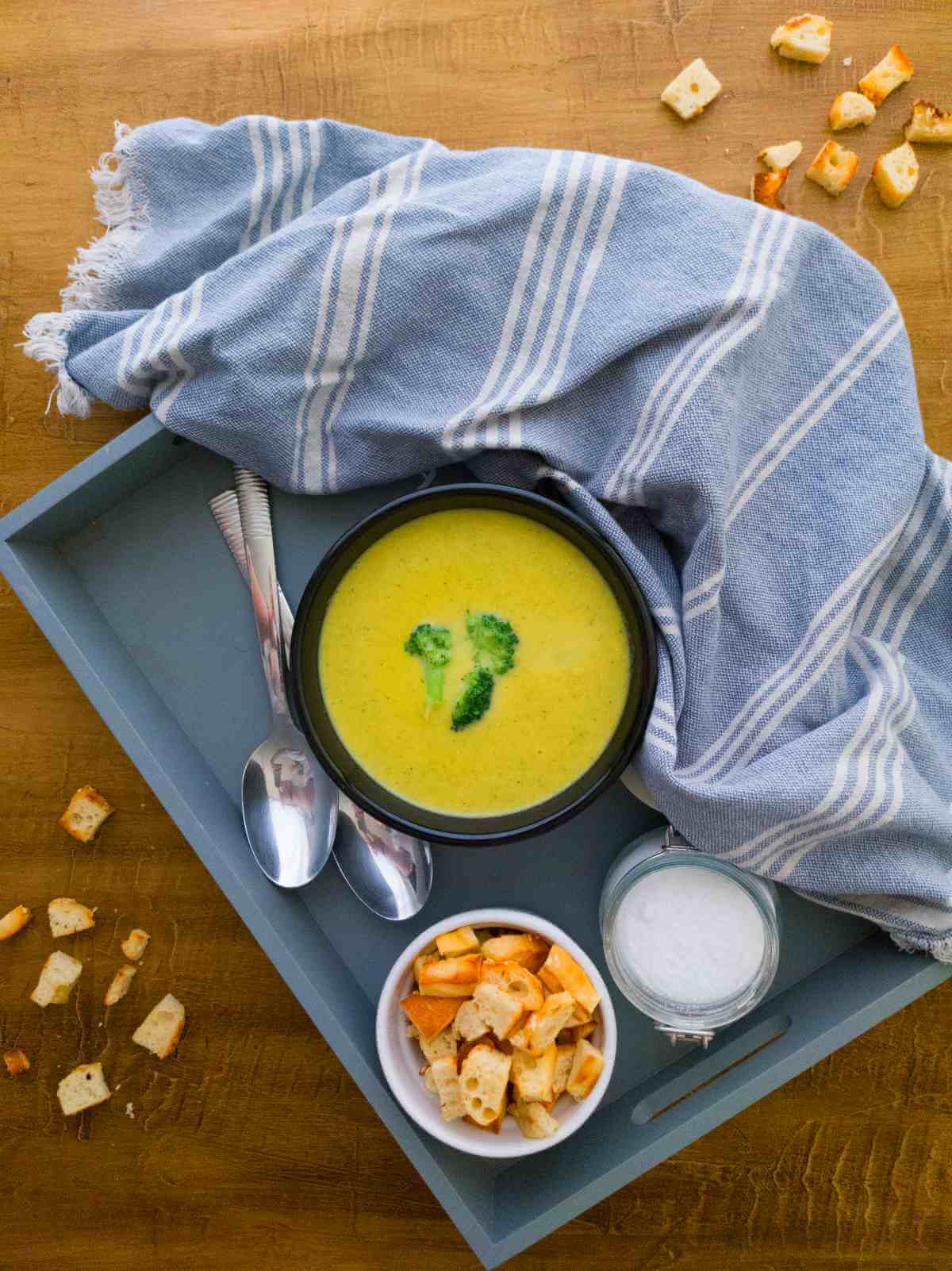Broccoli Cheddar Soup Vegan with croutons, spoons and a towel on a wooden surface.
