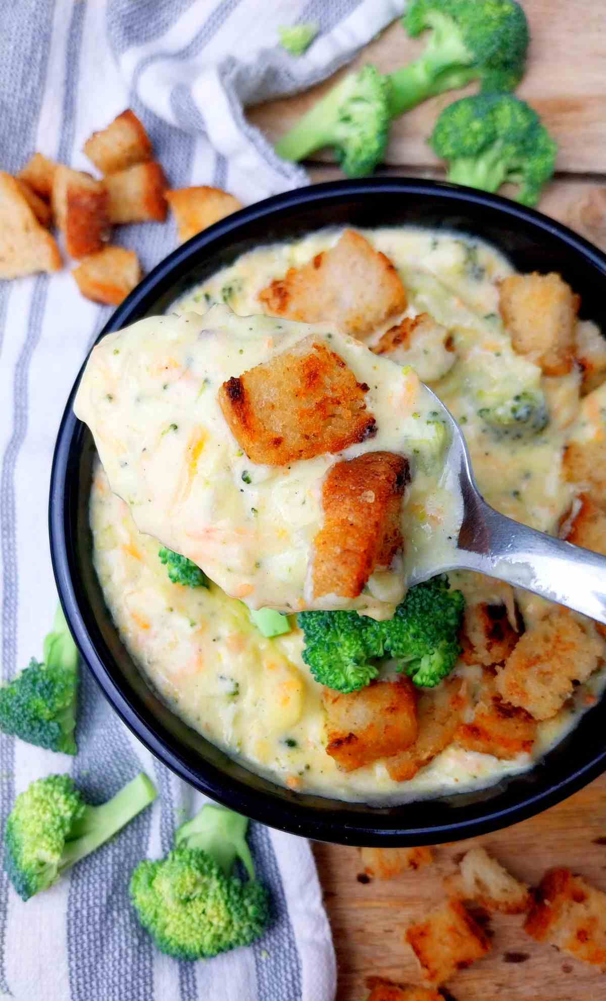 A bowl of homemade broccoli cheddar soup with a spoon full of soup with croutons.