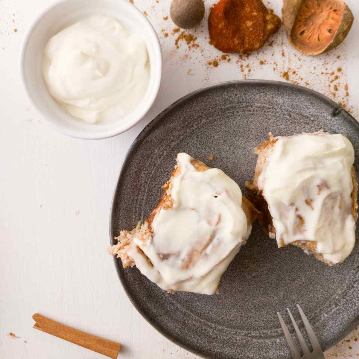 Gluten-free sourdough cinnamon rolls with cream cheese frosting on a plate with a fork.