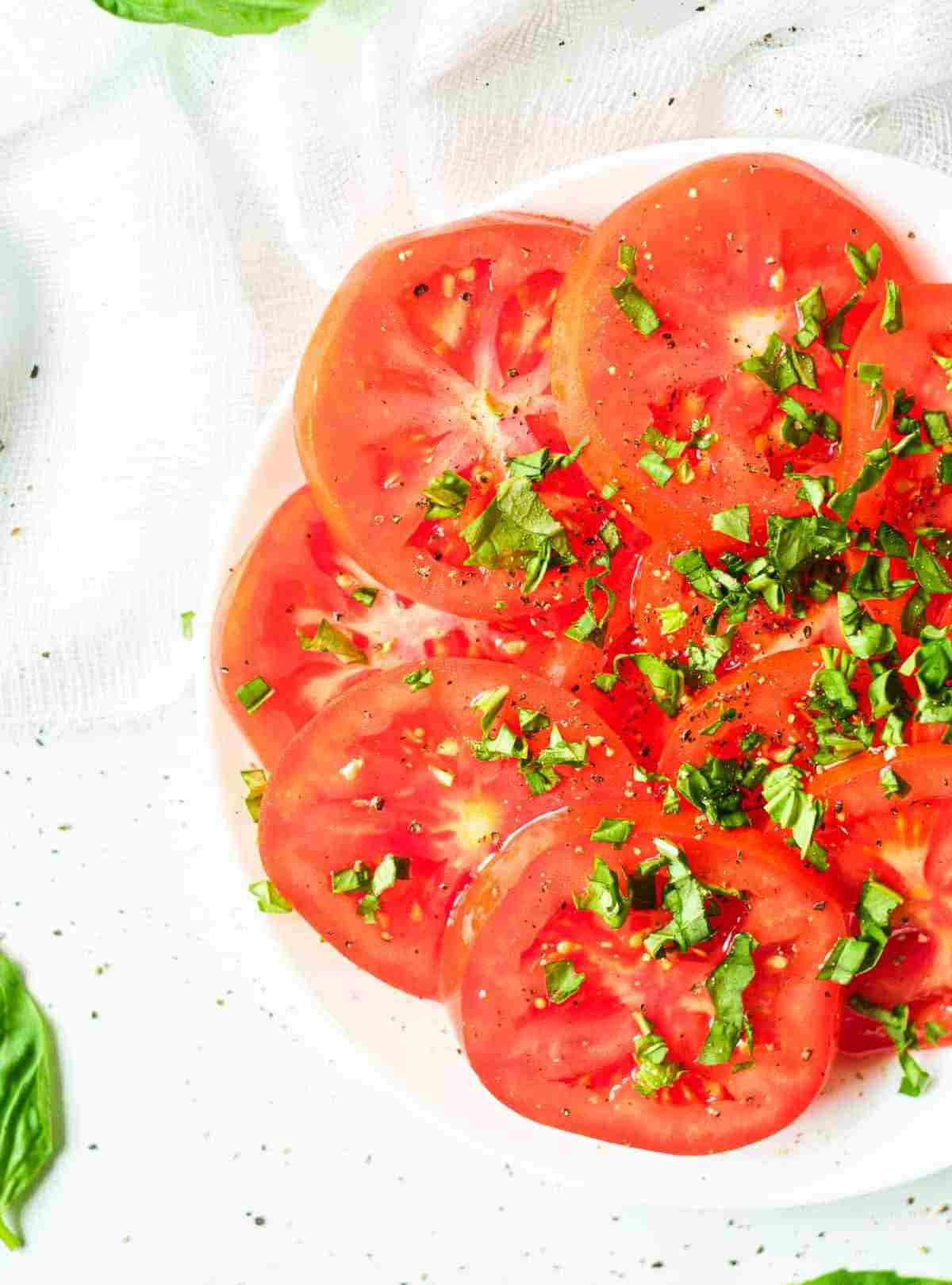 marinated tomatoes with greens on a white plate.