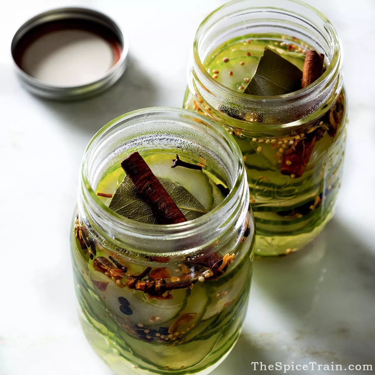 Homemade pickles in open mason jars on a white surface.