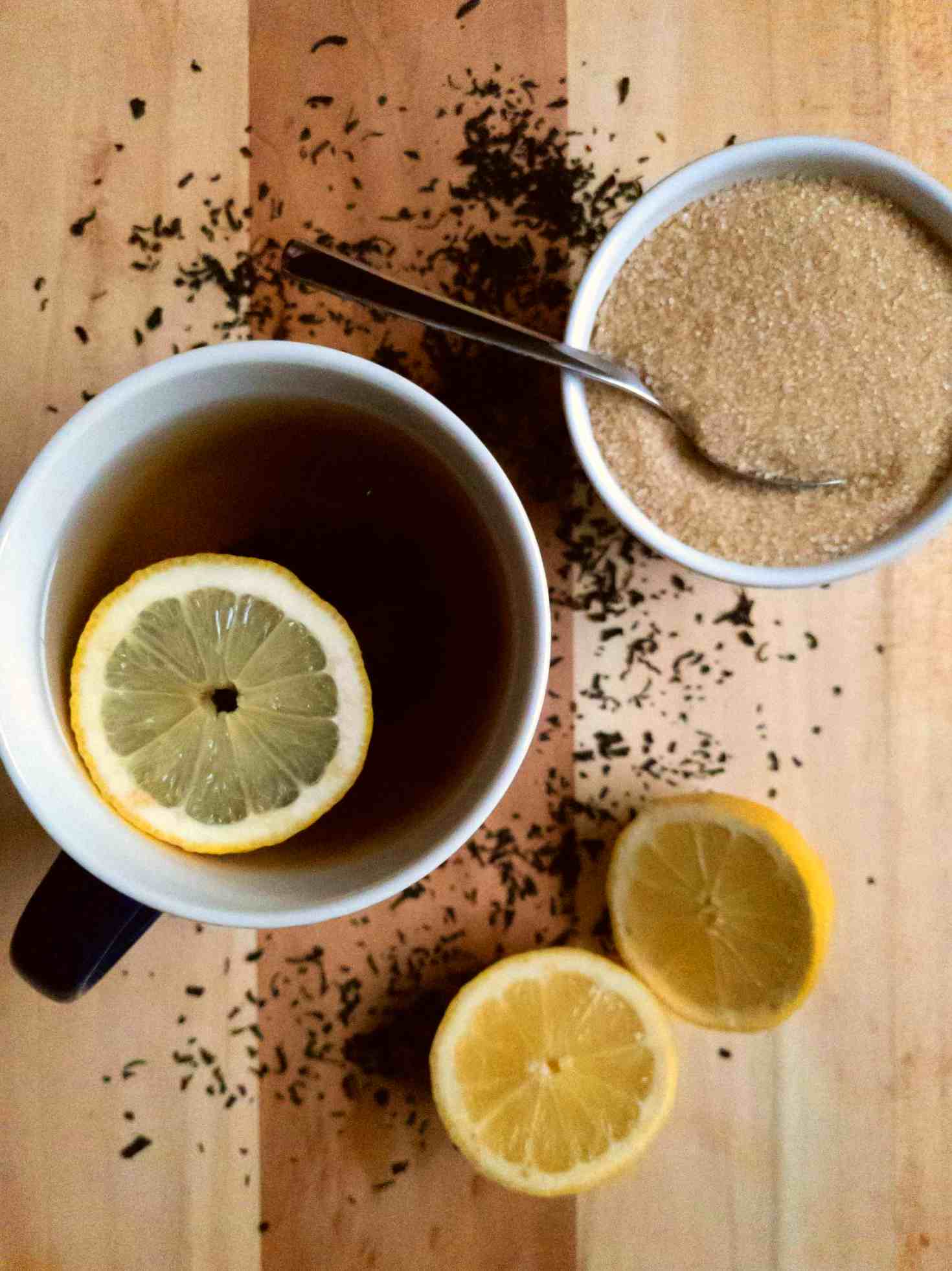 A cup of tea with lemon piece on top and sugar on the side.