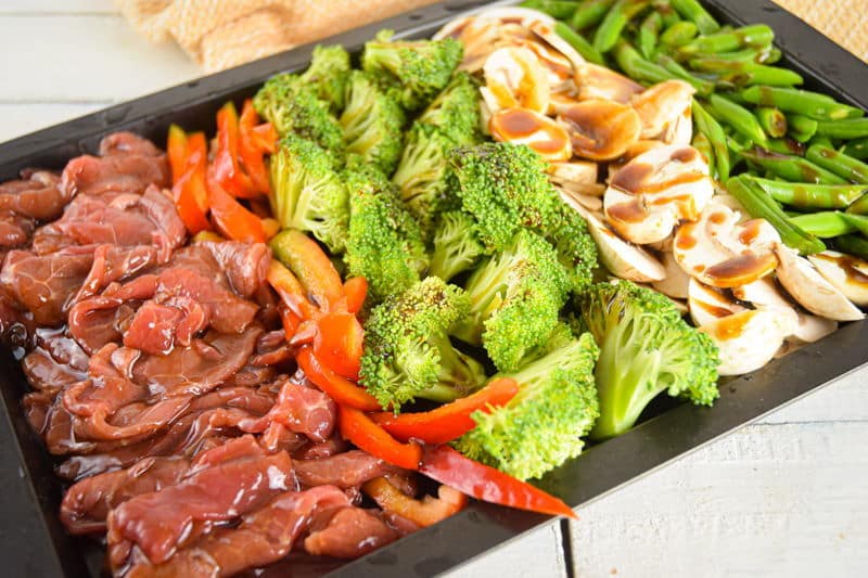 Raw beef, peppers, broccoli, and other veggies on a sheet pan.