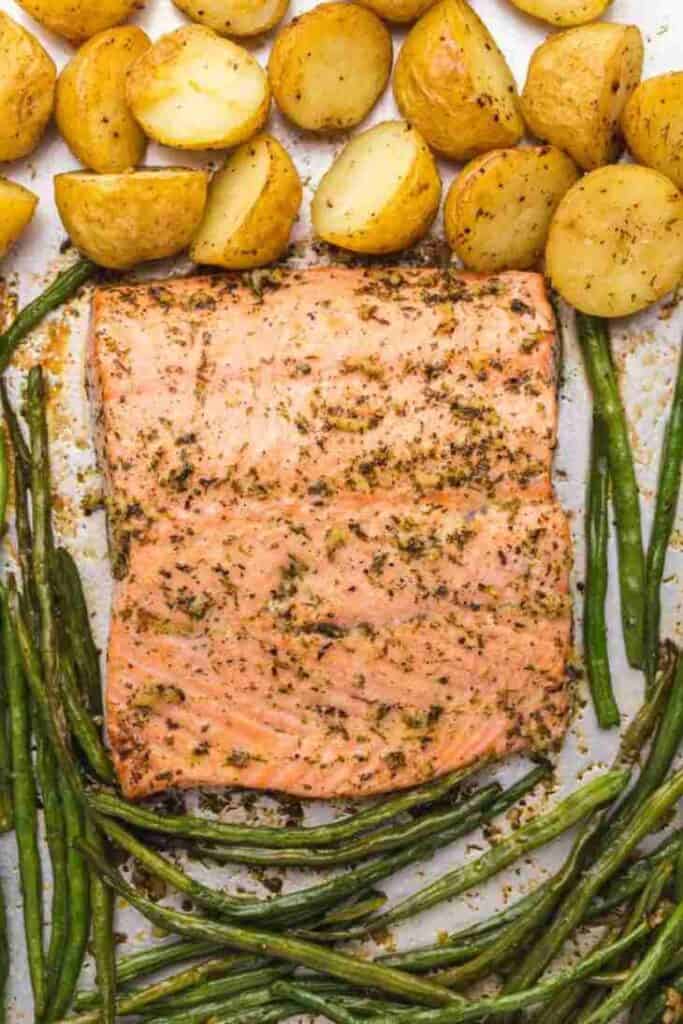 A large piece of salmon surrounded by potatoes and green beans on a tray.