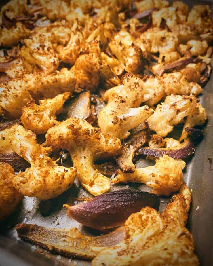 Cauliflower florets covered in tikka masala sauce on a sheet pan.