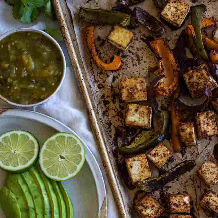 Baked Tofu and pepper slices on a tray next to a plate with lime, avocado, and a green sauce.