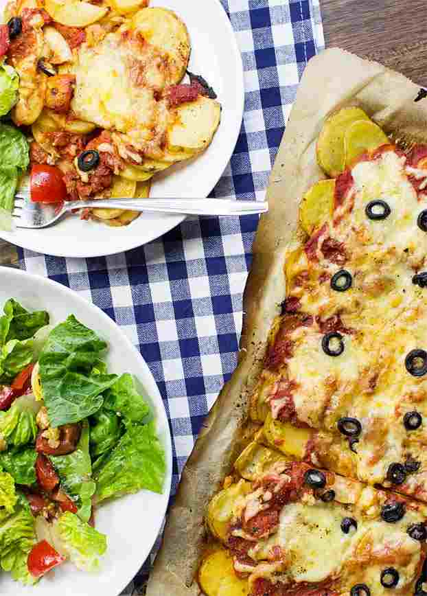 Pizza potatoes with olives on a tray next to a white plate with the pizza.