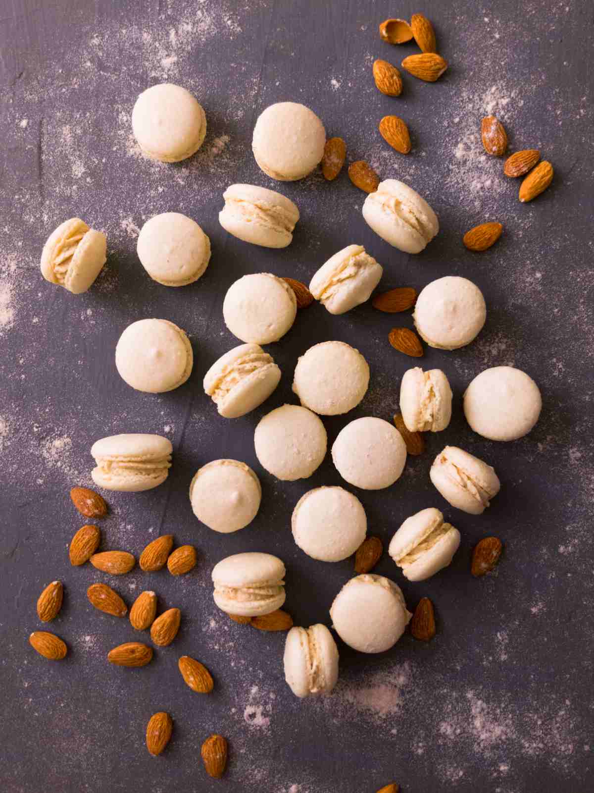 White dulce macarrons on a dark surface with almonds in the background.