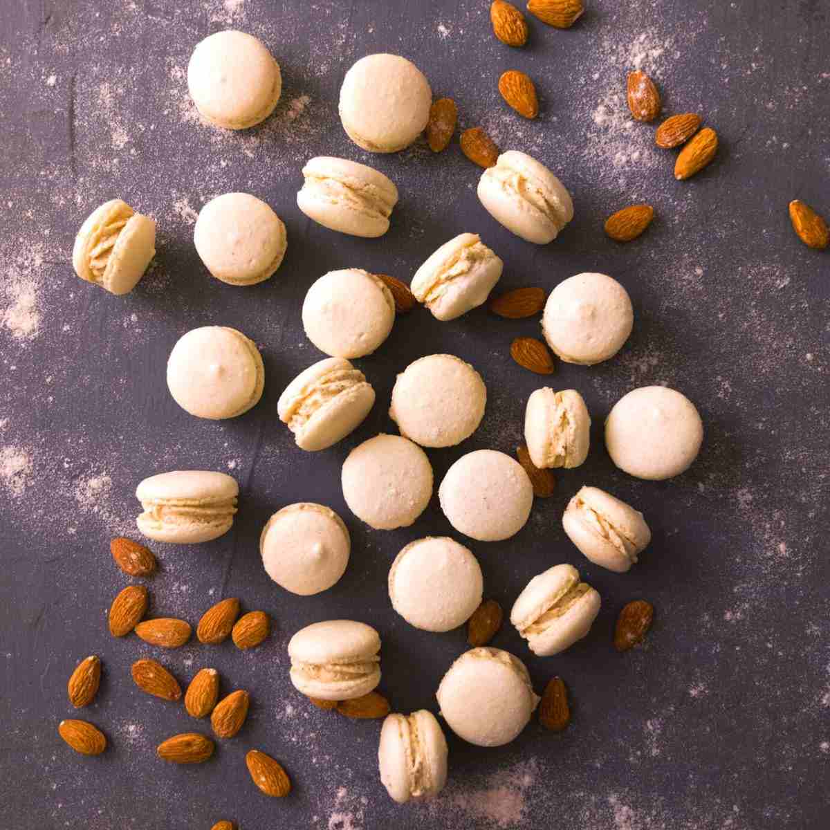 White macarons on a dark surface with almonds in the background.