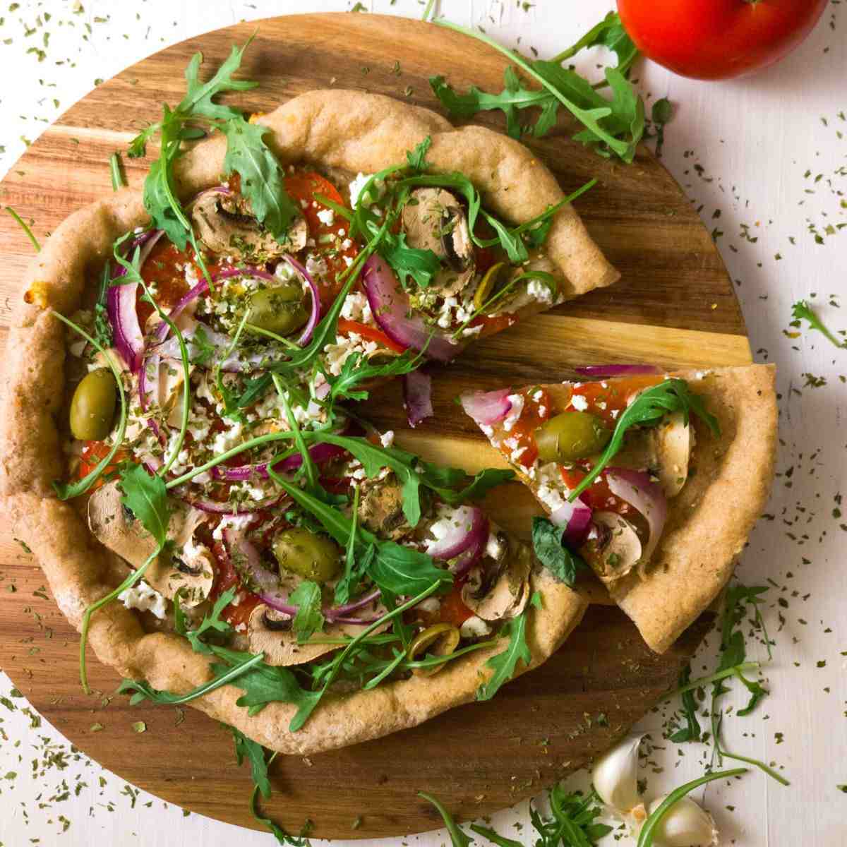 GF sourdough pizza with a slice cut out on a wooden board.