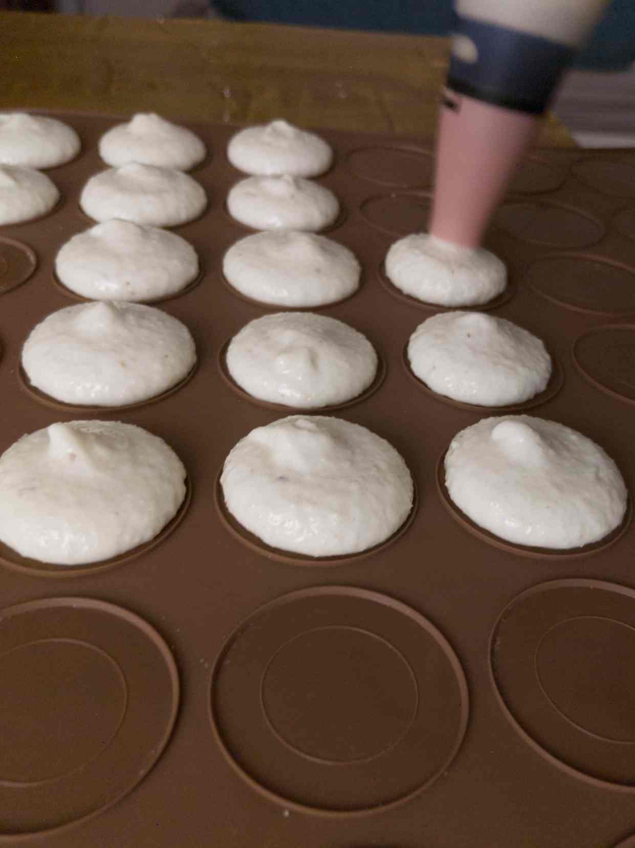 Piping macarons onto a silicone mat.