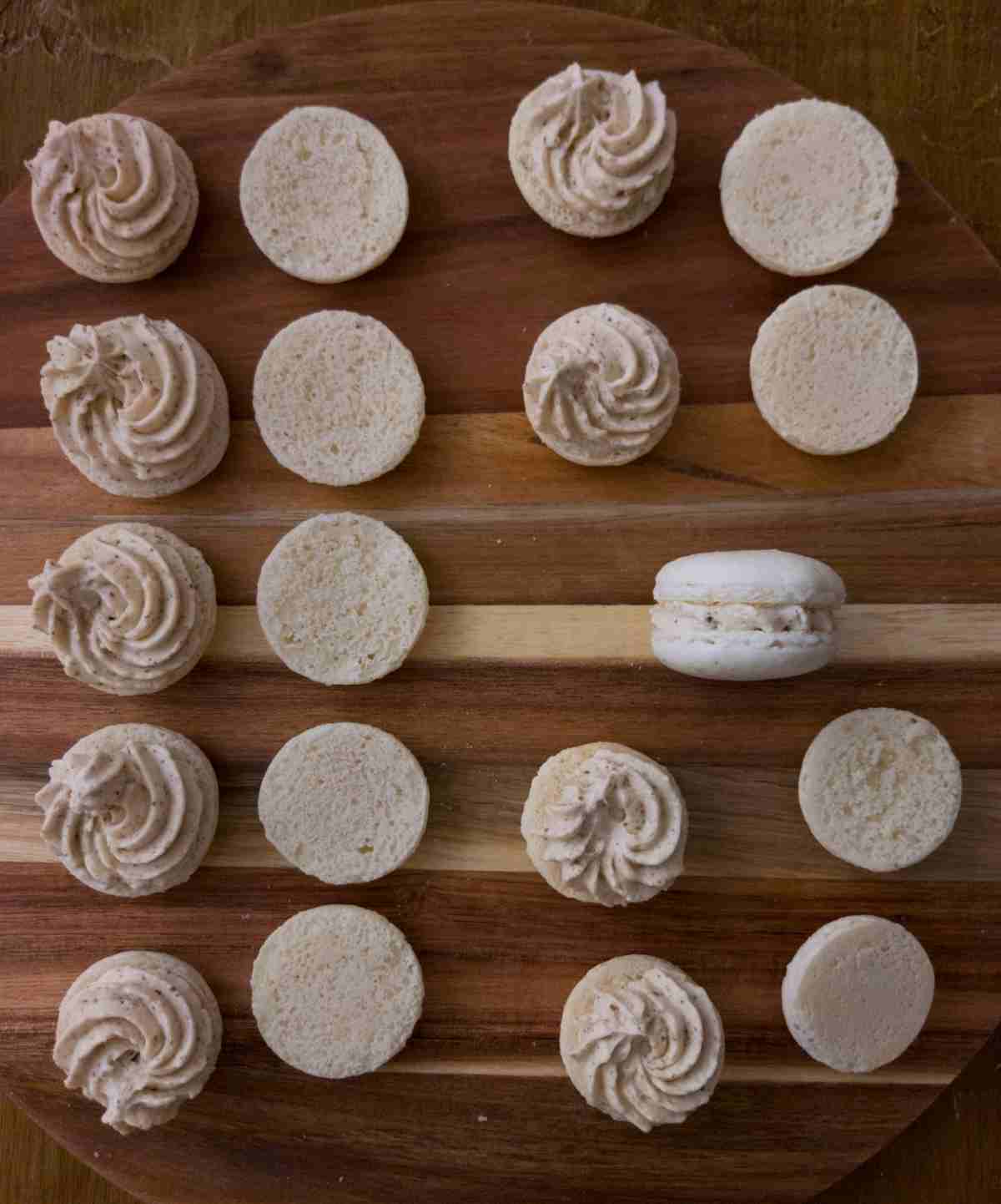 Macaron shells with buttercream on top on a wooden surface.